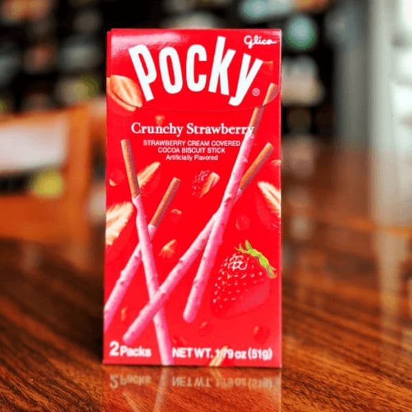 Red box of Glico Pocky Crunchy Strawberry biscuit sticks on a wooden table.