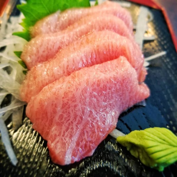 Close-up of five slices of pink fatty tuna sashimi with wasabi and shredded daikon.