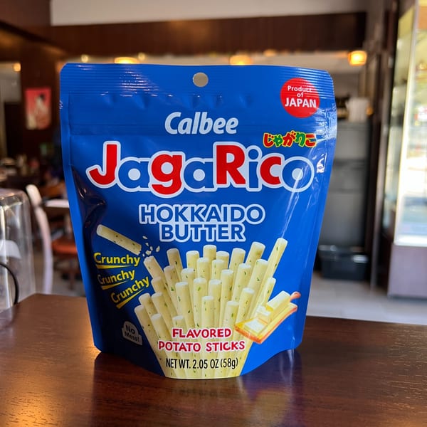 A blue bag of Calbee JagaRico Hokkaido Butter flavored potato sticks sits on a wooden table.