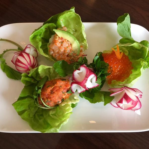 Sushi Chef's lettuce wraps with various fillings and carved radishes on a white plate.