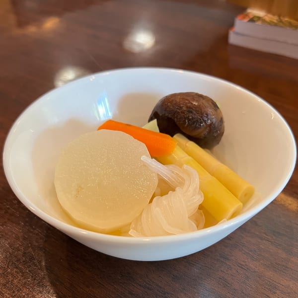 A white bowl of Japanese simmered vegetables, including daikon, carrots, bamboo shoots, and a mushroom.