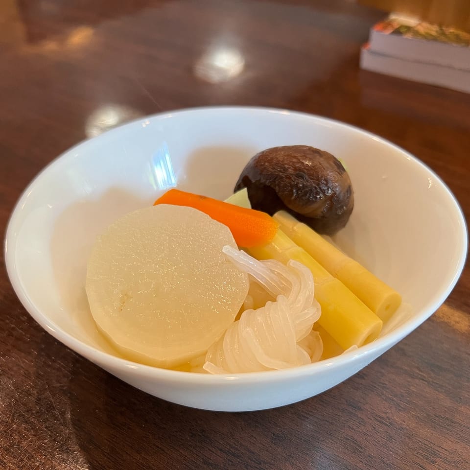 A white bowl of Japanese simmered vegetables, including daikon, carrots, bamboo shoots, and a mushroom.