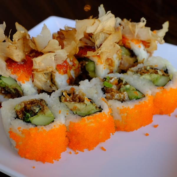 Sushi rolls with orange roe, avocado, and crispy toppings on a white plate.