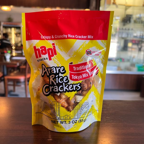A yellow and red bag of Hapi Snacks Arare Rice Crackers, Traditional Tokyo Mix, on a wooden table.