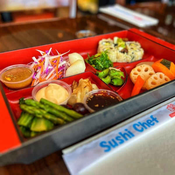 A Sushi Chef bento box filled with sushi rolls, lotus root, asparagus, salad, and sauces.